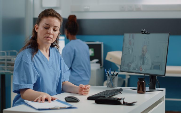 Nurse using video call for conversation with doctor on computer. Medical assistant talking to medic on online video conference for remote advice and telemedicine while sitting in cabinet